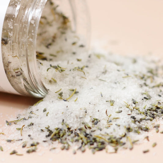 Close up of bath salts, white salts with pieces of rosemary and lavender.