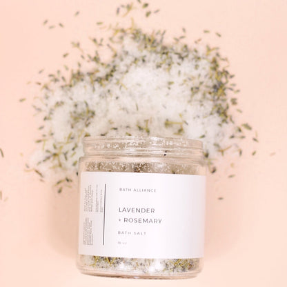 Bath salts jar (clear with white label saying "Lavender + Rosemary" and bath salt mixture of white salts with lavender and rosemary pieces mixed in.