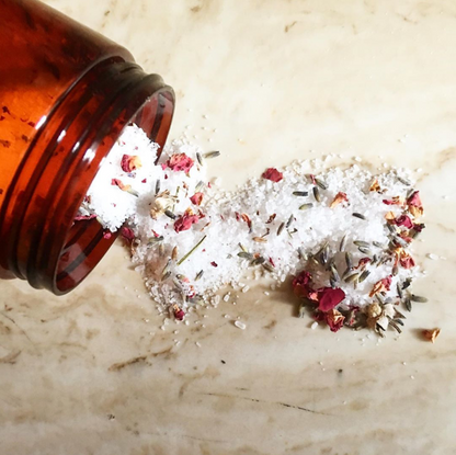 Bath Soak mixture of white powder, flower petals and lavender spilling out of dark red jar.